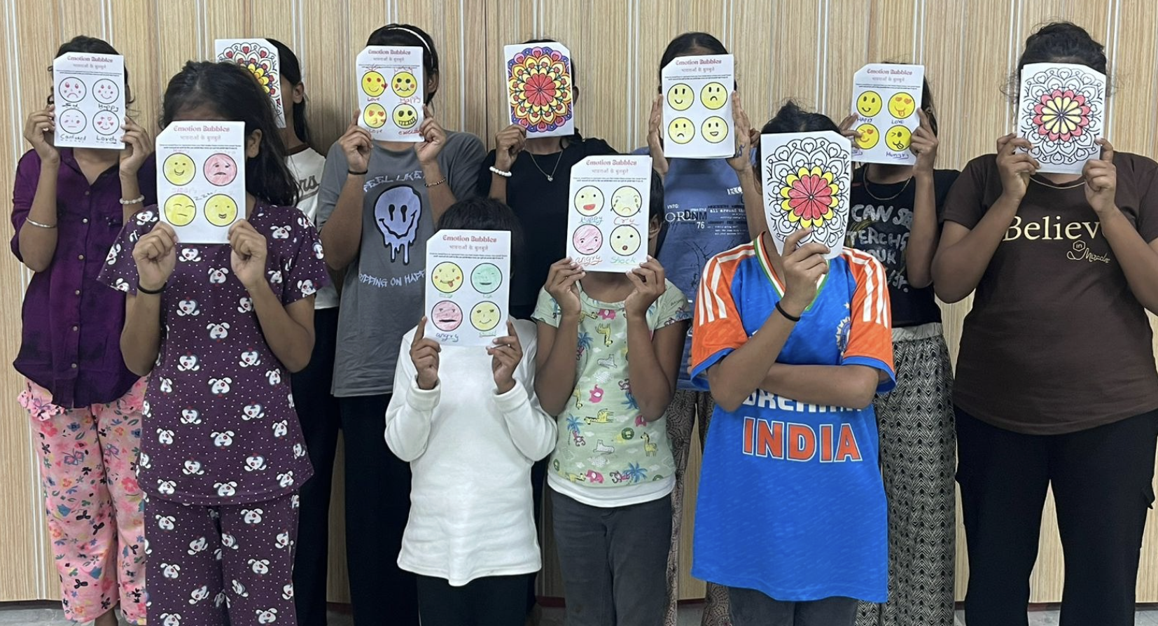Students holding up emotion worksheets and mandalas at Asha Kiran NGO