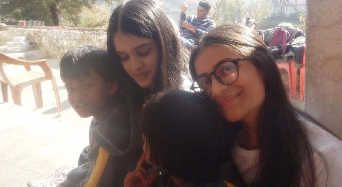 Two members of the Healing Hearts Foundation team sitting close with two schoolchildren outdoors at Bangloo Ki Kandi Government School in Mussoorie.