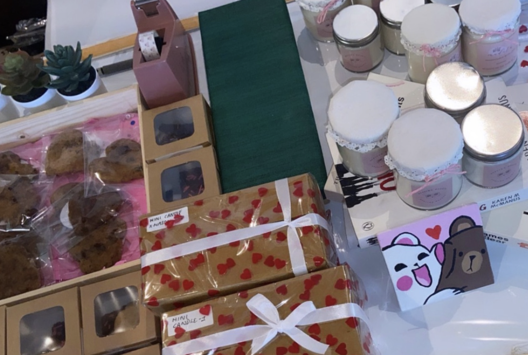Close-up of the Healing Hearts Foundation stall table at the Unveiled Exhibition, showing wrapped gifts, candle jars and packaged cookies.