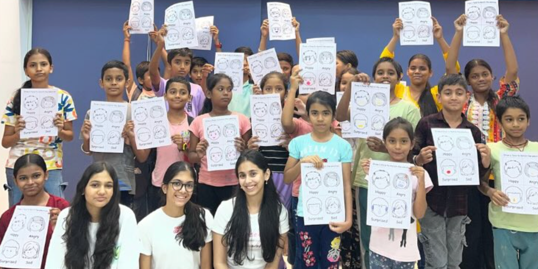 Children and facilitators holding emotion worksheets at Raksha NGO
