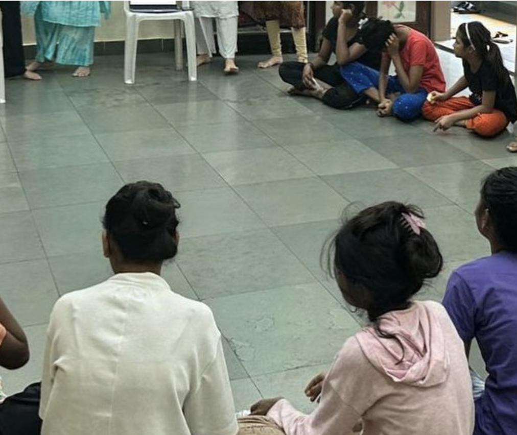 Girls and young women of Asha Kiran NGO sitting together in a circle on the floor during the reusable sanitary pad donation session.